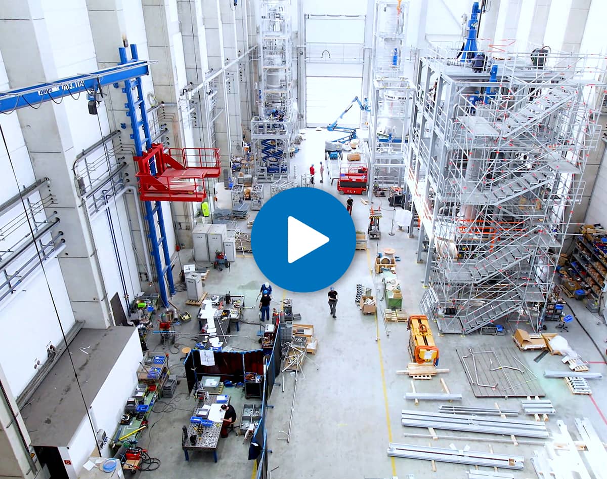 overview of manufacturing plant with white play button on blue circle